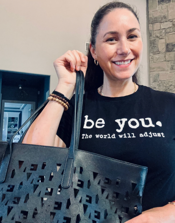 Jenn Greenhut holding a Love, Zero Negative tote bag, wearing a "be you. The world will adjust" t-shirt