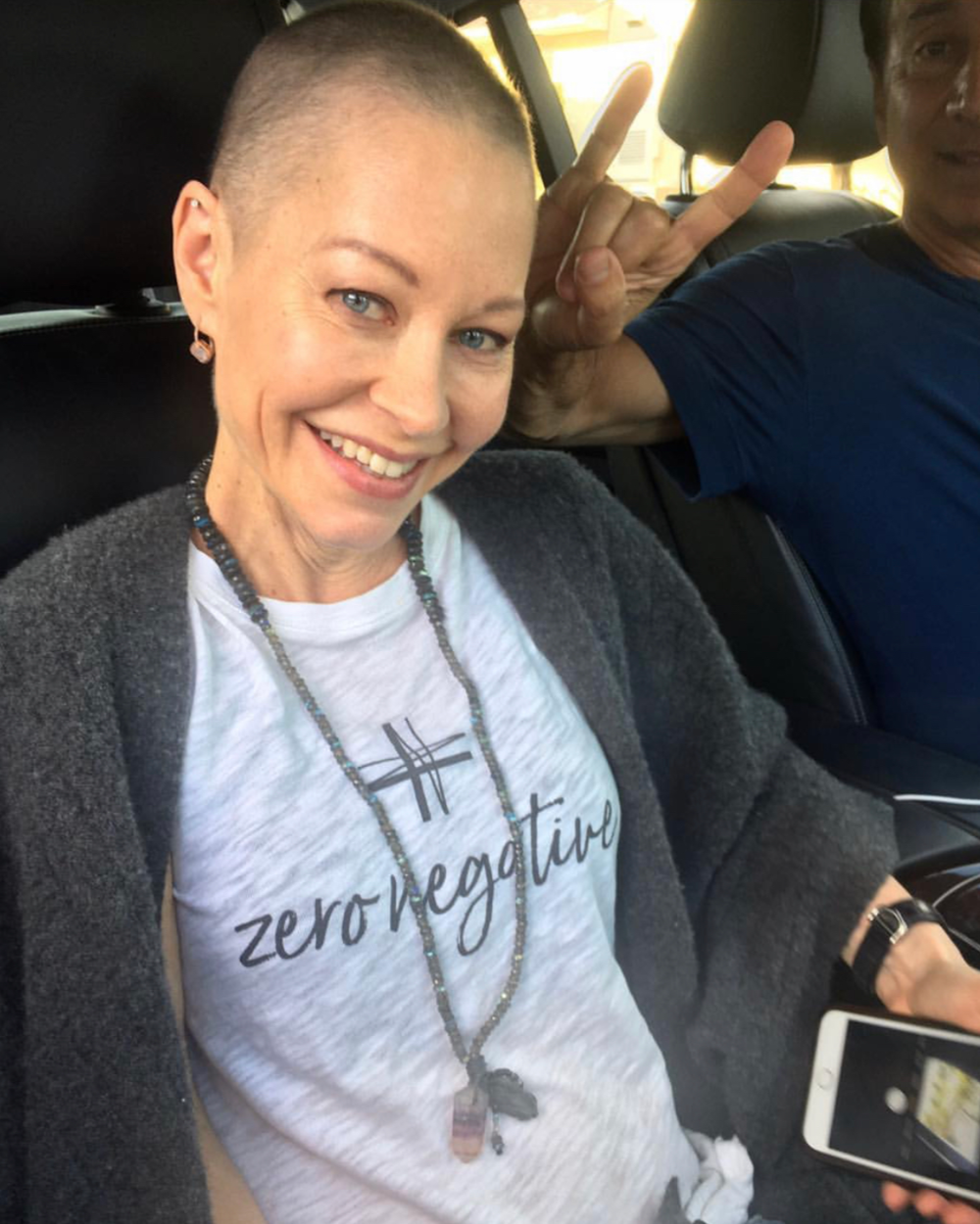 Person with a shaved head wearing a 'zero negative' shirt in a car.